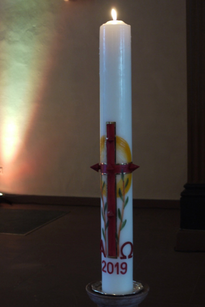 Die neue Osterkerze mit einem großem roten Kreuz und den Buchstaben A und O  ist entzündet